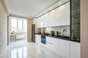 one wall kitchen ideas featuring a modern white gloss kitchen with sleek handleless cabinets, marble-effect backsplash, black countertop, built-in appliances, recessed ceiling lights, and a bright open layout.