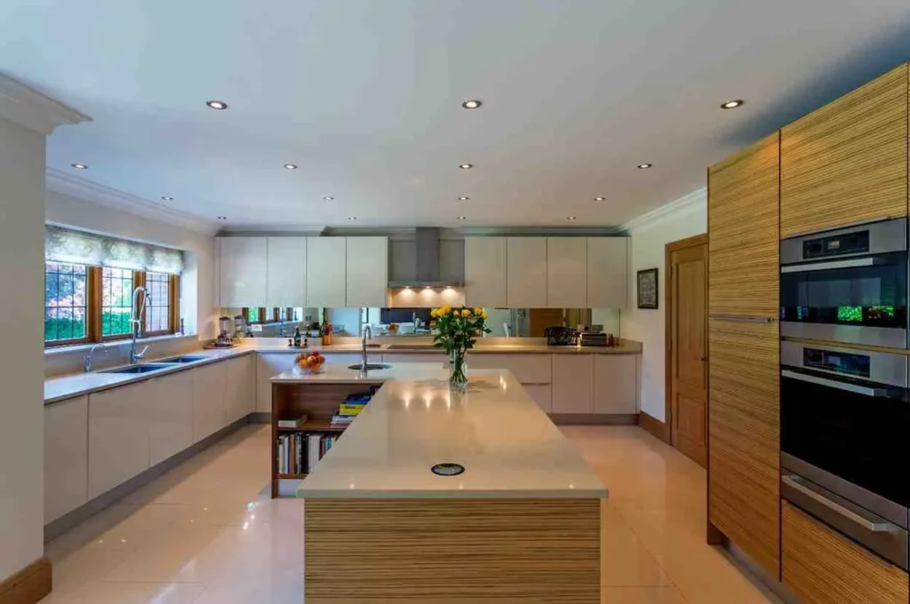Open Plan Kitchen Ideas: Modern open plan kitchen with a large central island, sleek white cabinets, built-in ovens, wood accents, and a spacious layout ideal for family living and entertaining.