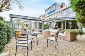 Rear House Extension Ideas featuring a modern glass rear extension with an open-plan kitchen extension, large sliding doors, contemporary outdoor seating, and a stylish UK home design.
